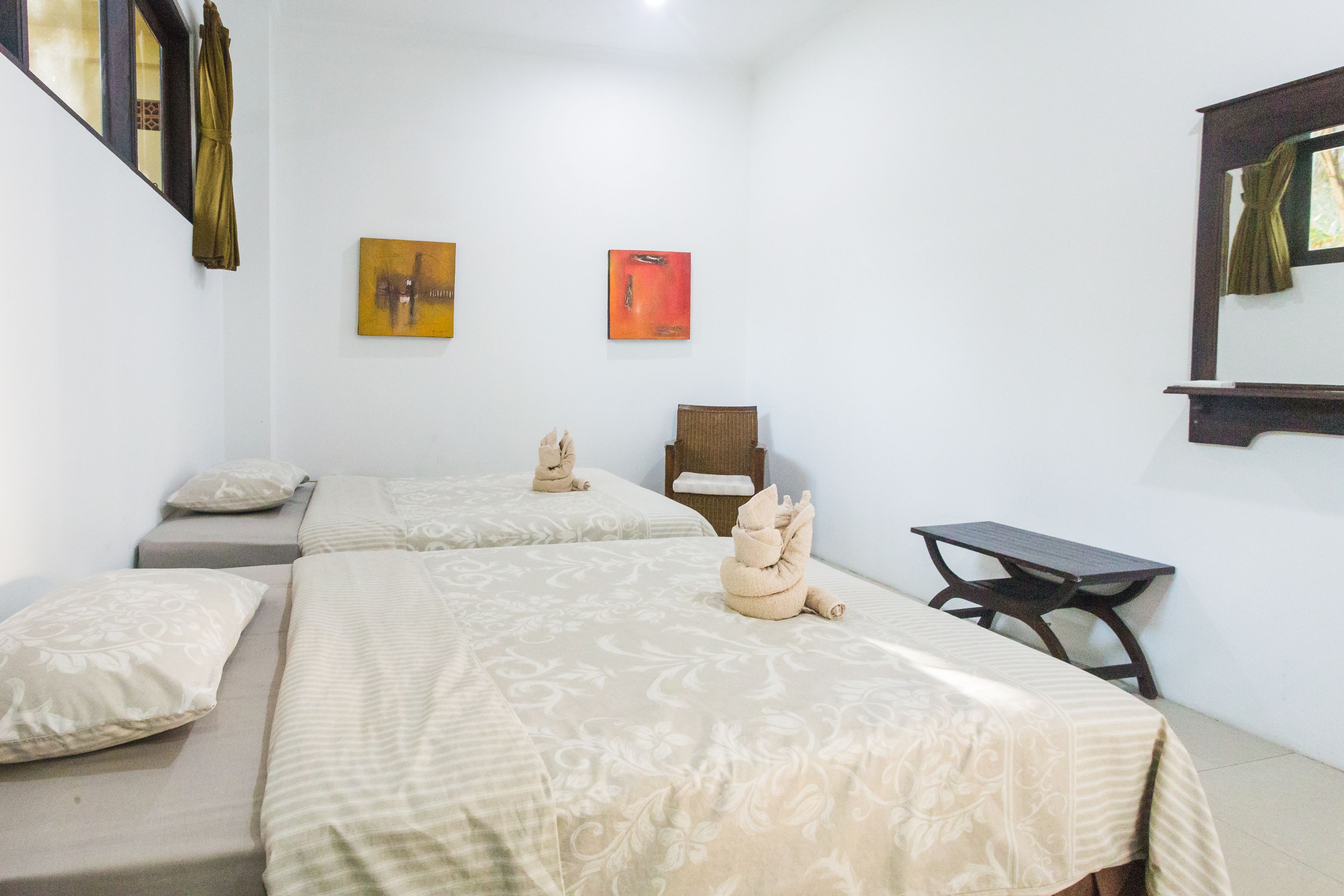 Habitación de hotel con dos camas, una mesita y dos sillas. Hay dos cuadros en la pared.