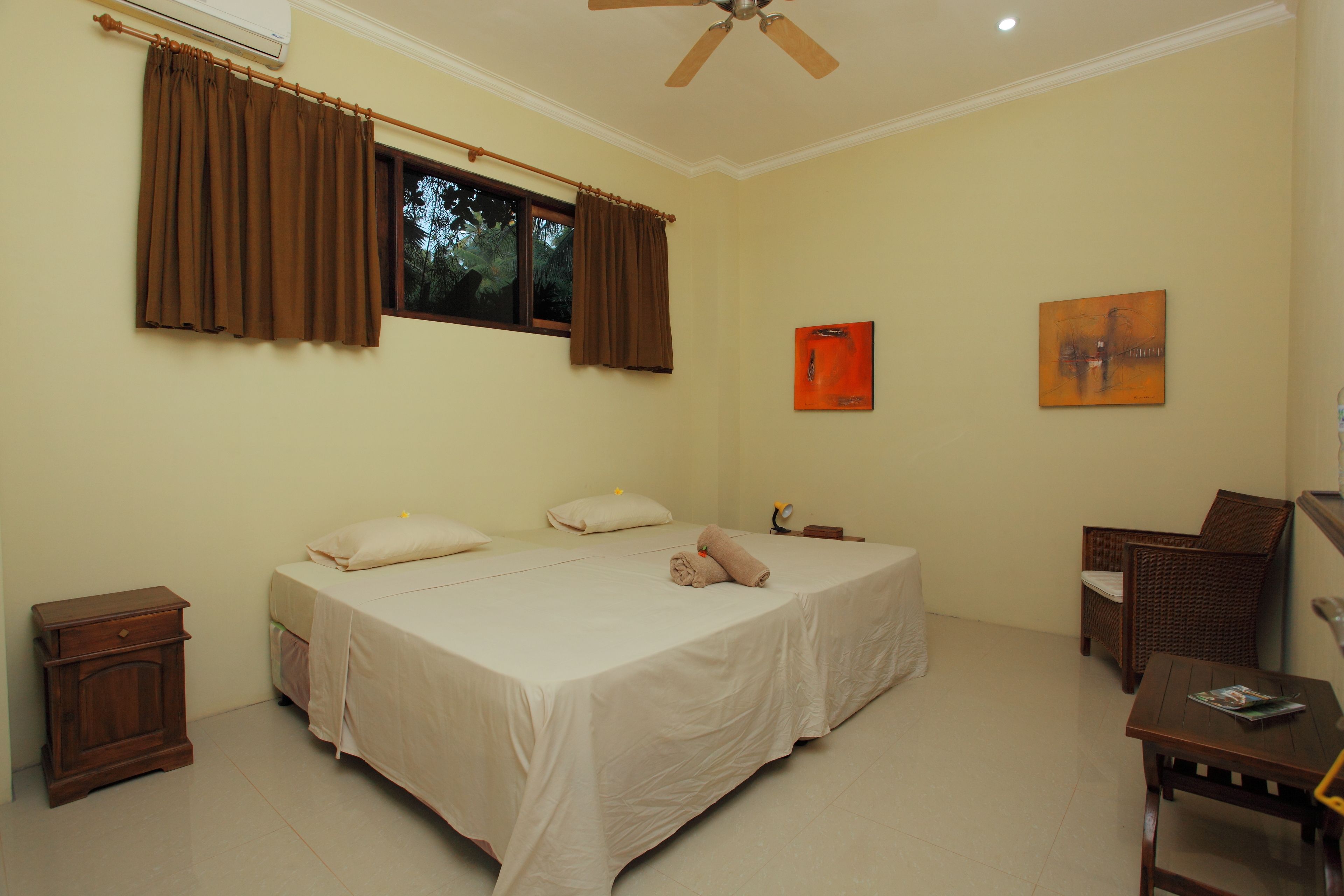 A bedroom with a bed, a nightstand, a chair, and two paintings on the wall.