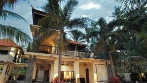 Ein zweistöckiges Gebäude mit Balkon, Pool und umliegenden Palmen.