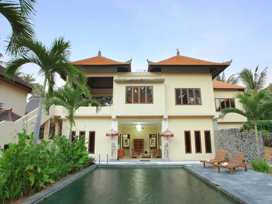Una casa de dos pisos con piscina, terraza de madera y plantas tropicales.