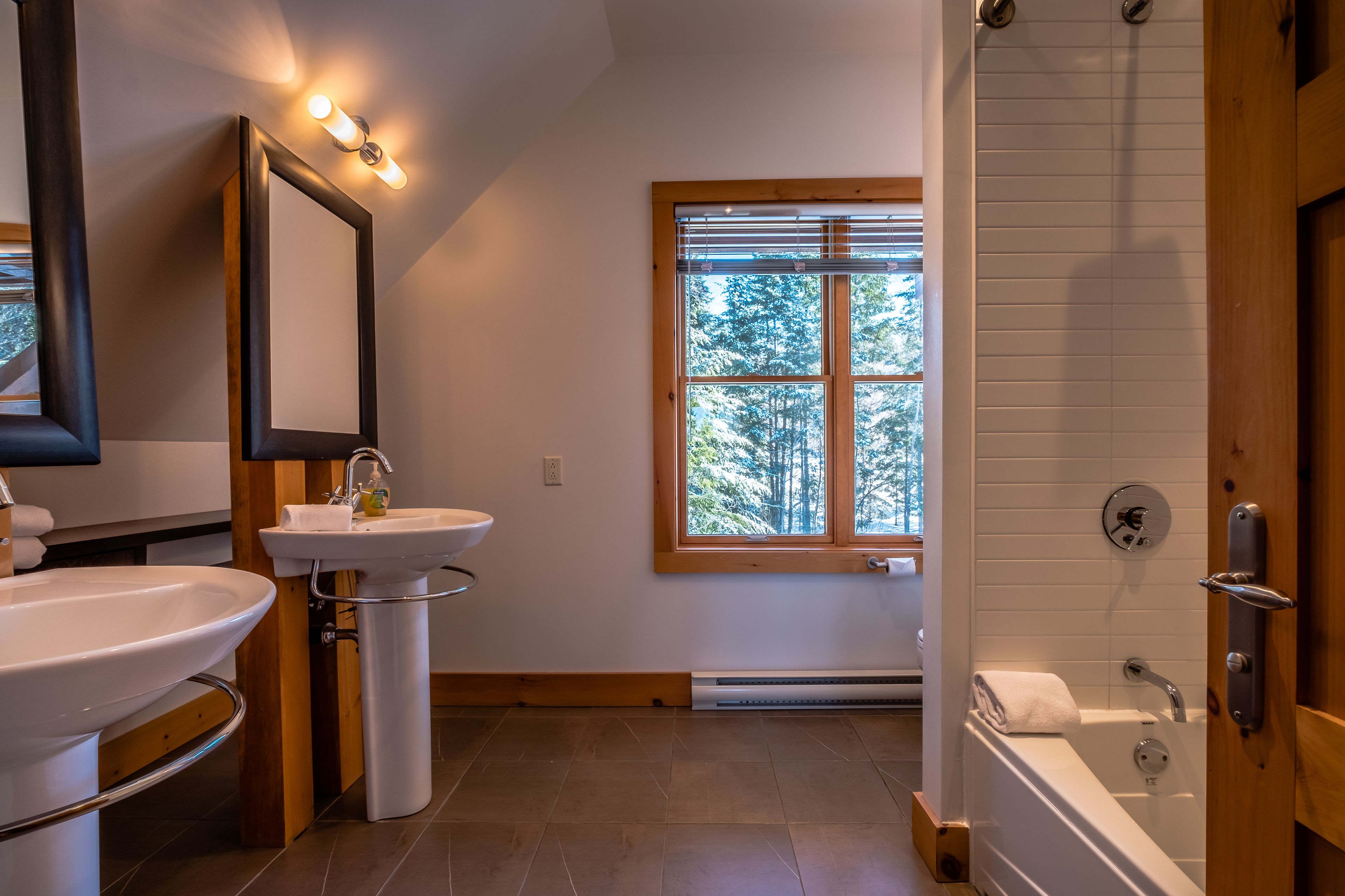 A bathroom with two sinks, a large mirror, a window with blinds, and a bathtub.