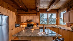 A modern kitchen with granite countertops, wooden cabinets, stainless steel appliances, and a large island with seating. - RCNT Chalets (Lac-Superieur)