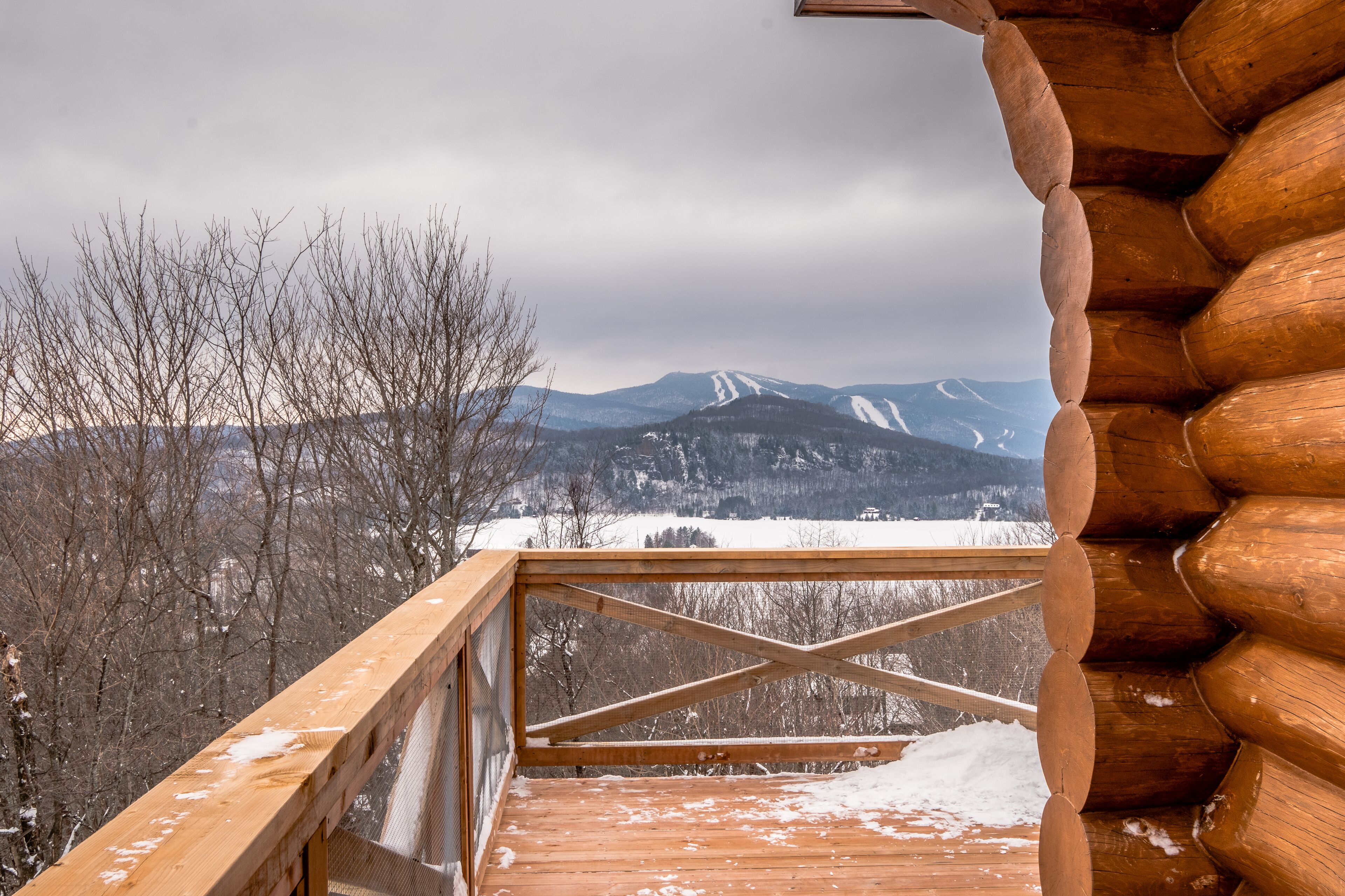 Una terraza de madera con vistas a montañas y árboles nevados.