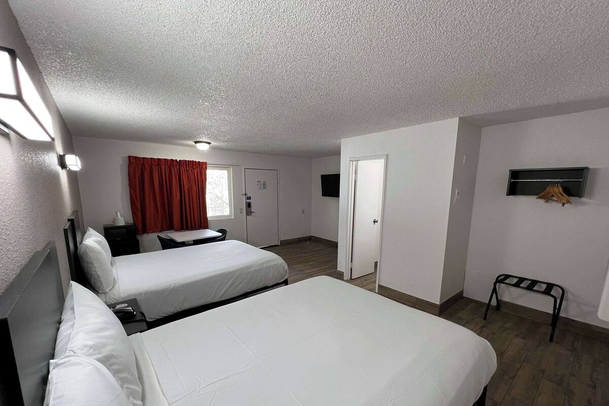 A hotel room with two beds, a small table, a chair, a TV mounted on the wall, and a coat rack.