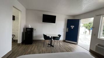 A hotel room with a bed, a desk with a chair, a microwave, a TV mounted on the wall, and a door with the number 203.