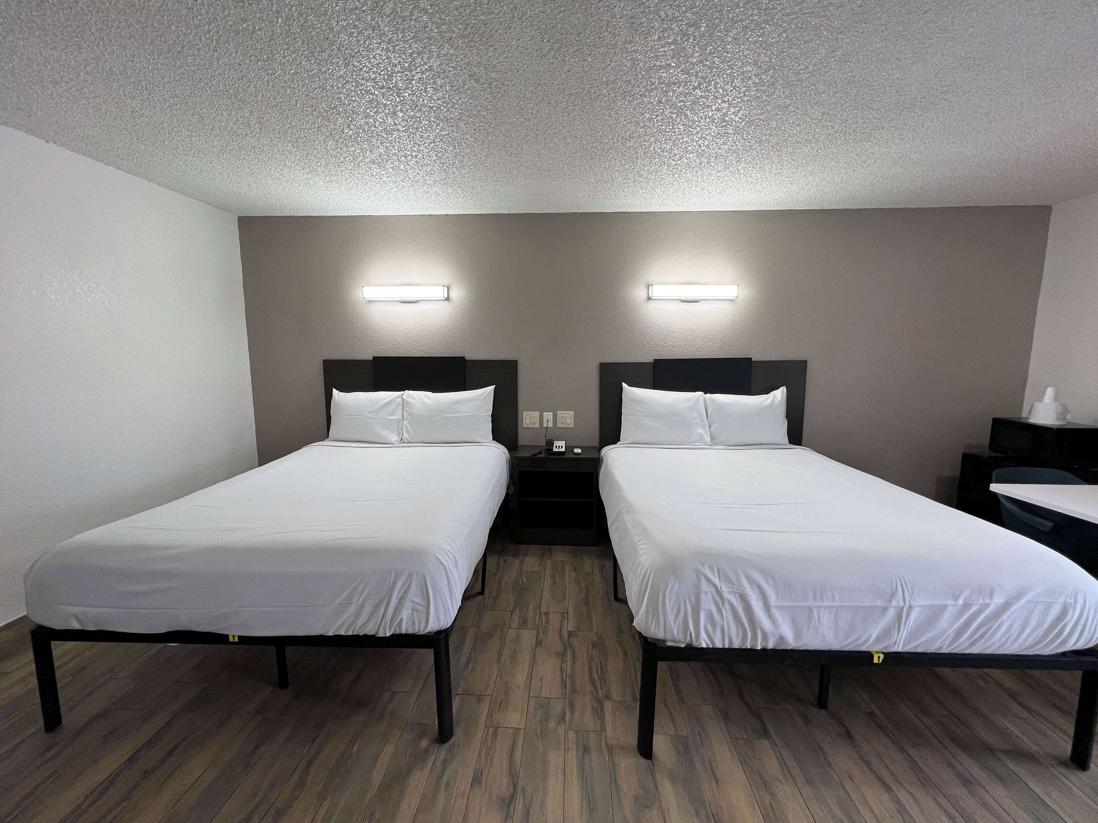 Una habitació d'hotel amb dos llits individuals, una tauleta de nit amb un telèfon i una taula petita amb una tassa.