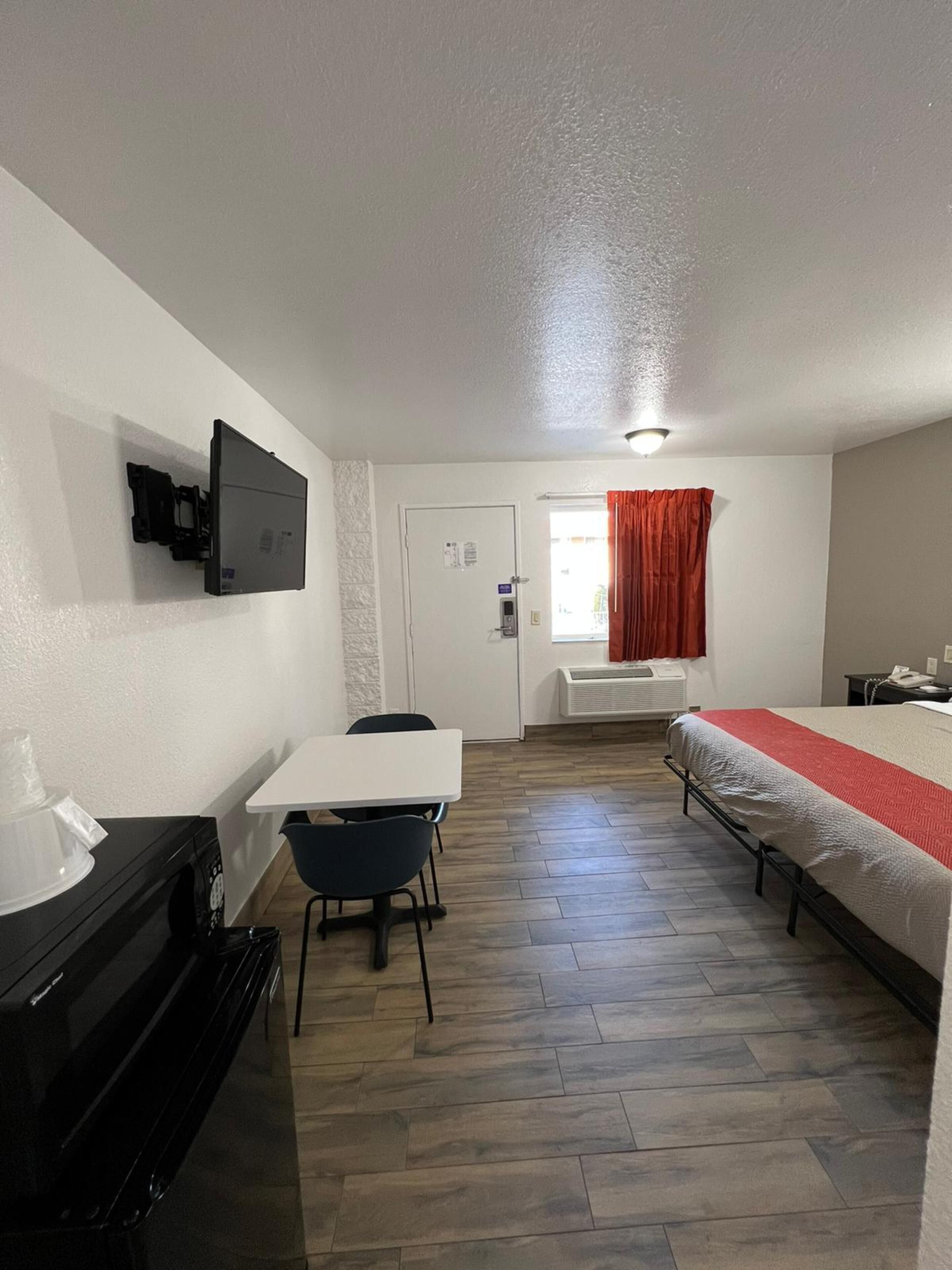 A compact hotel room with a bed, a desk, a chair, a TV mounted on the wall, and a window with curtains.