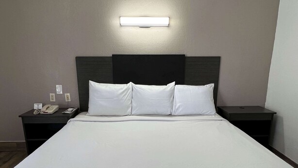 A hotel room with a large bed, two bedside tables, a nightstand, and a wall-mounted light. - Motel 6 Orange, CA - Anaheim (Orange)
