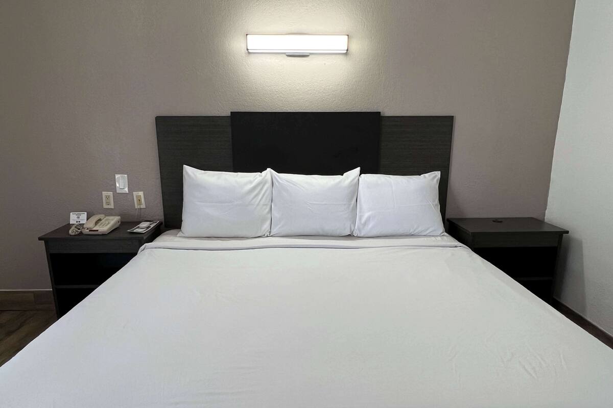 A hotel room with a large bed, two bedside tables, a nightstand, and a wall-mounted light.