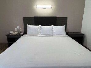 Une chambre d’hôtel avec un grand lit, deux tables de chevet, une petite table et une lampe fixée au mur.
