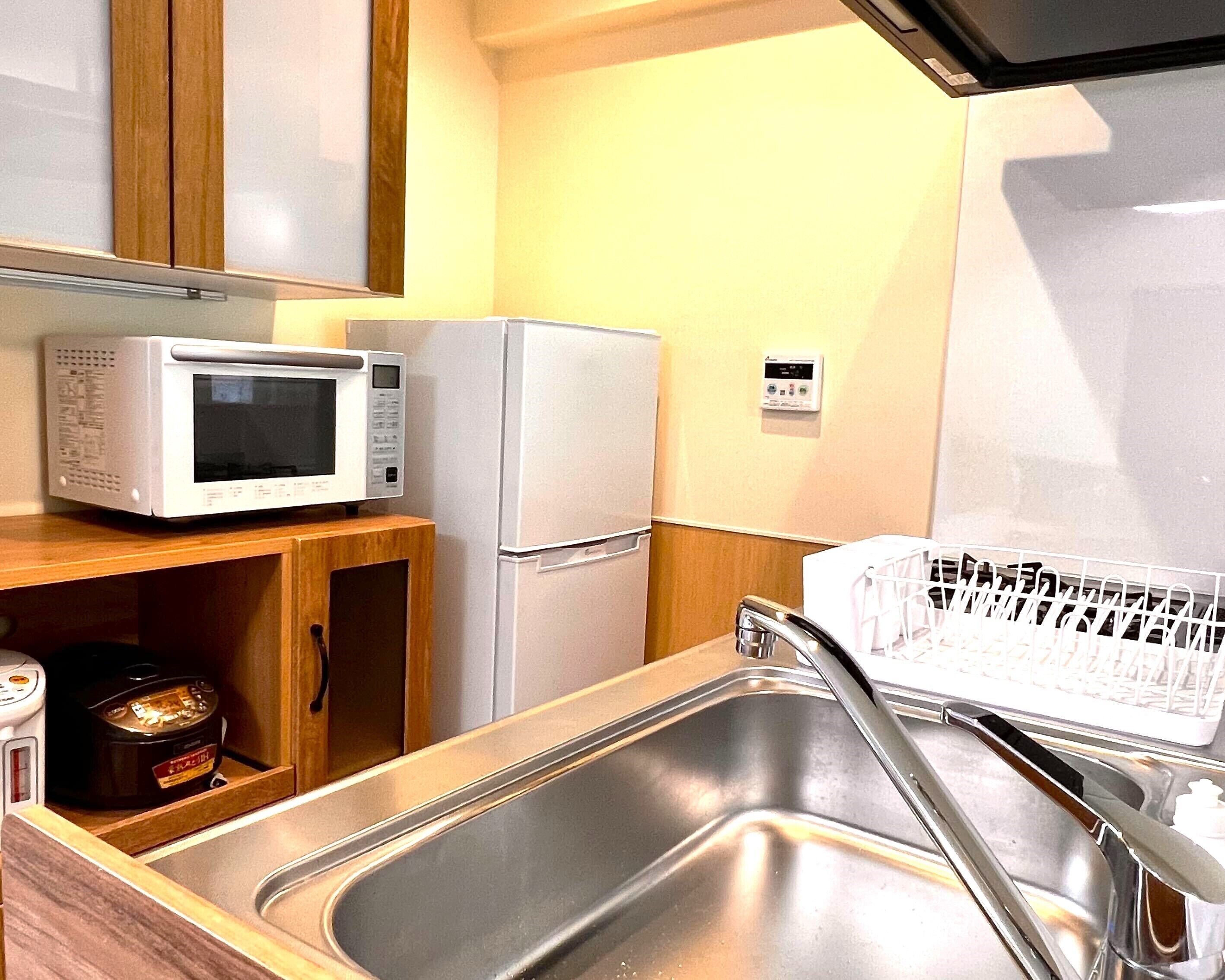 A compact kitchen with a microwave, refrigerator, and stainless steel sink.