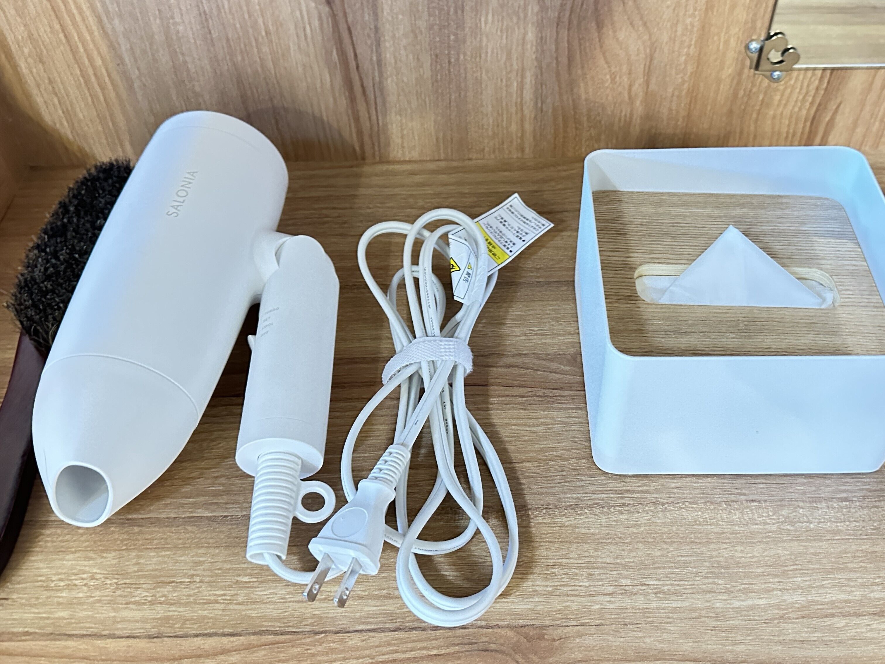 Un secador de pelo, un cable de alimentación y un adaptador de corriente sobre una superficie de madera.
