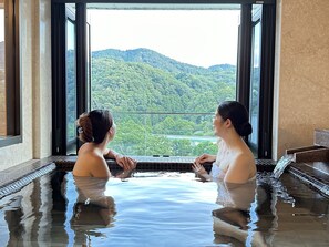 Zwei Personen in einer Hot-Whirl-Badewanne mit Blick auf einen bewaldeten Berg.