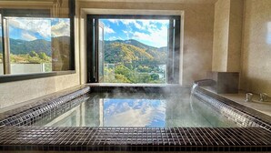 A hot tub with a view of a mountainous landscape through a large window. - Condominium Hotel Garland Court Usami (Ito)