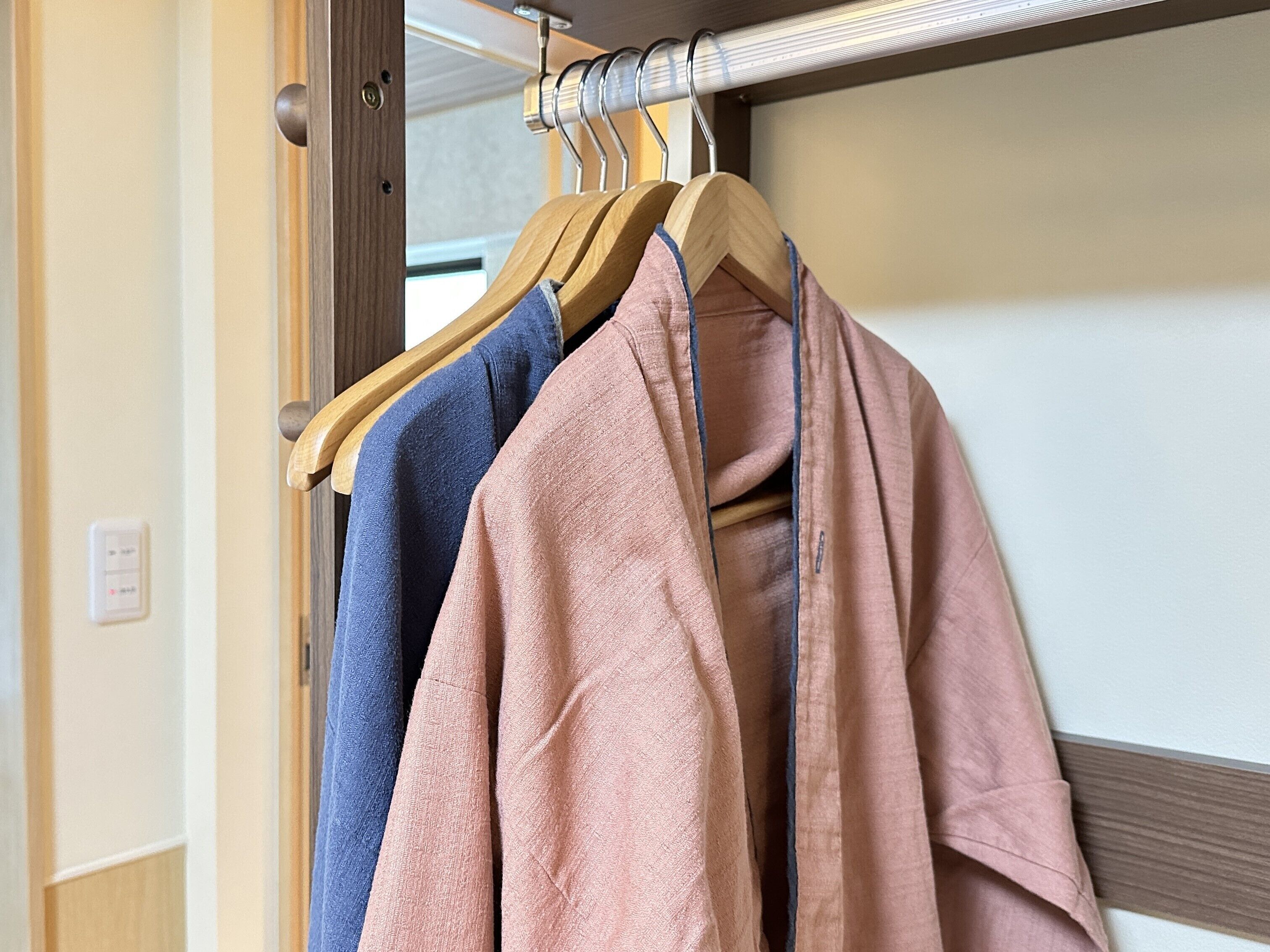 A wooden hanger with three towels in shades of blue, pink, and beige.