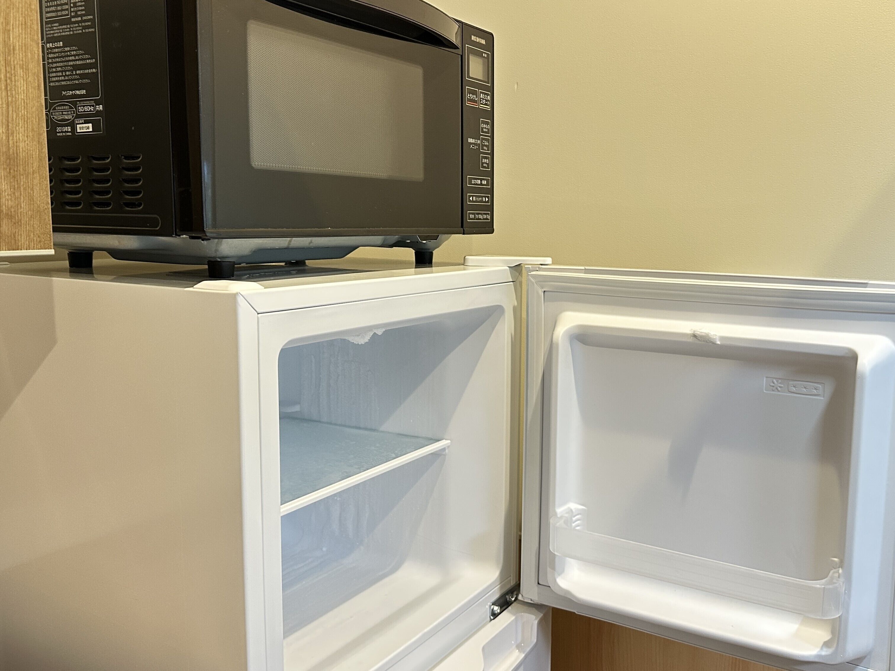 A compact refrigerator with a microwave on top, a freezer compartment, and a control panel with buttons and a display.