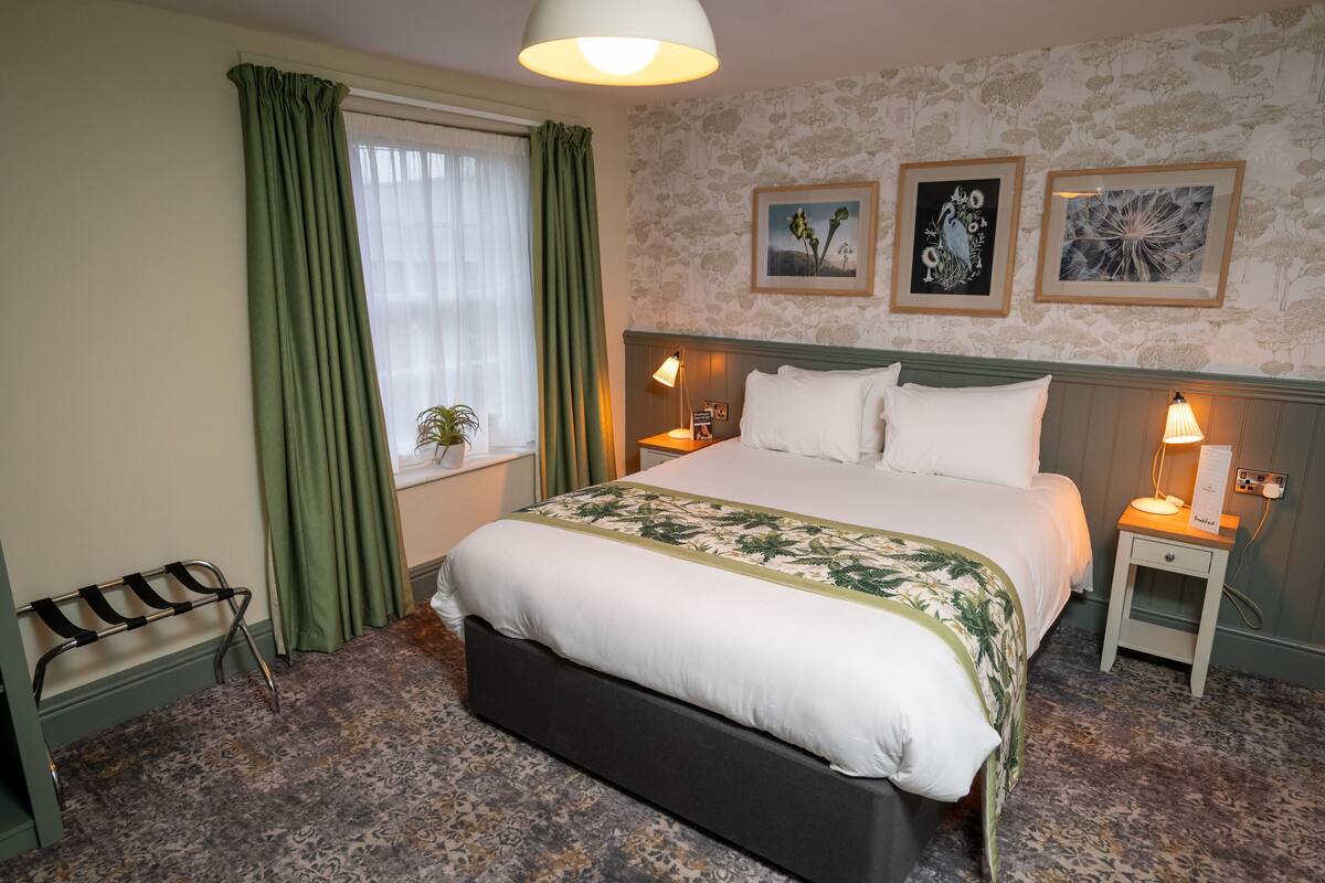 A neatly arranged bedroom with a large bed, two bedside tables with lamps, a bench, and a window with curtains.