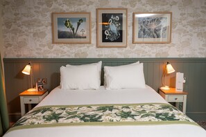 A neatly made bed with white linens and a green floral bedspread, flanked by two bedside tables with lamps and framed artwork on the wall.