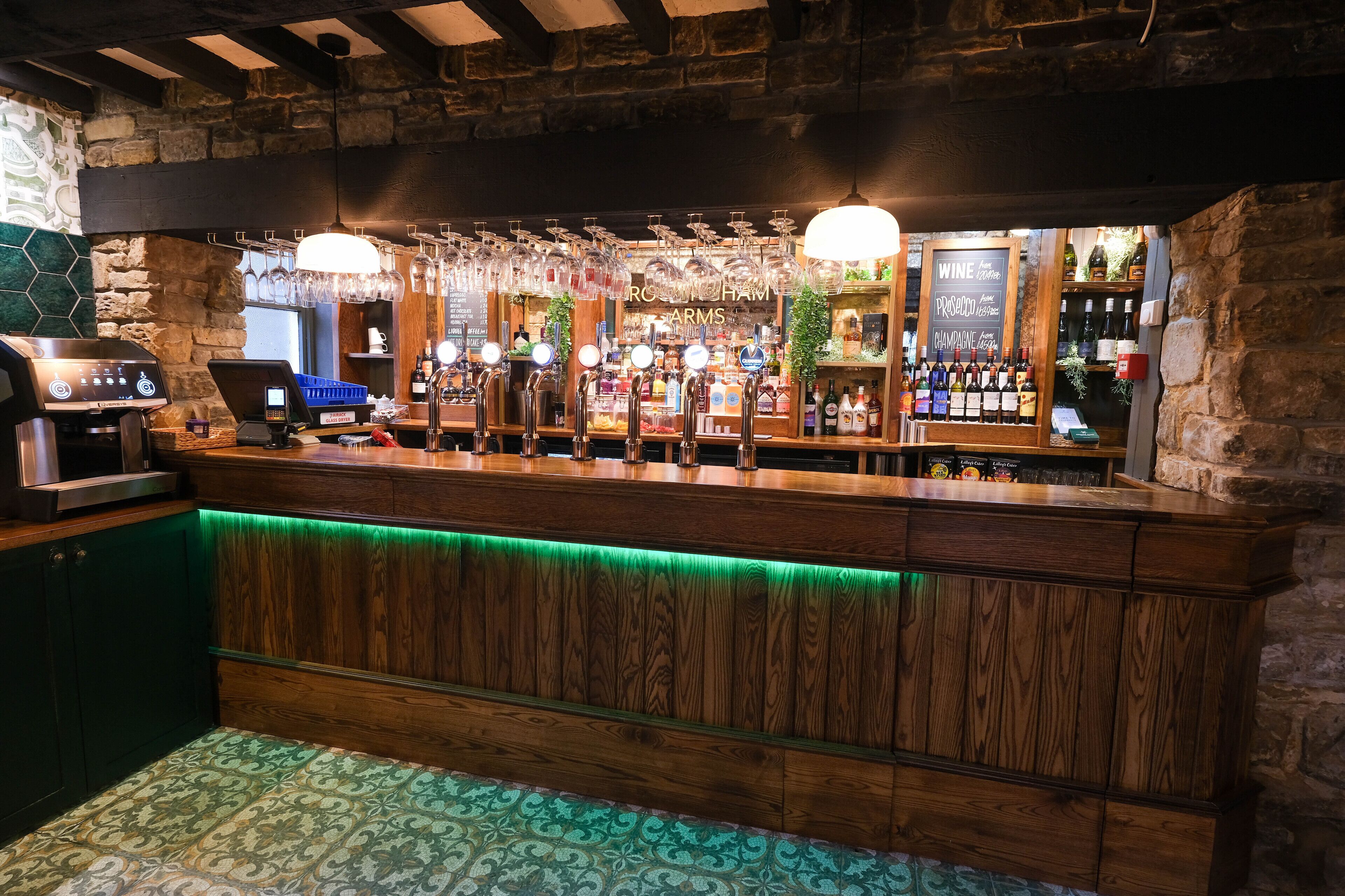 Una zona de bar con mostrador de madera, varias llaves y una variedad de botellas y vasos.