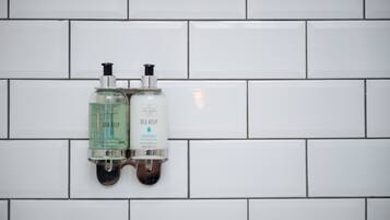 Dos dispensadores de jabón de manos fijos en una pared de azulejos blancos.