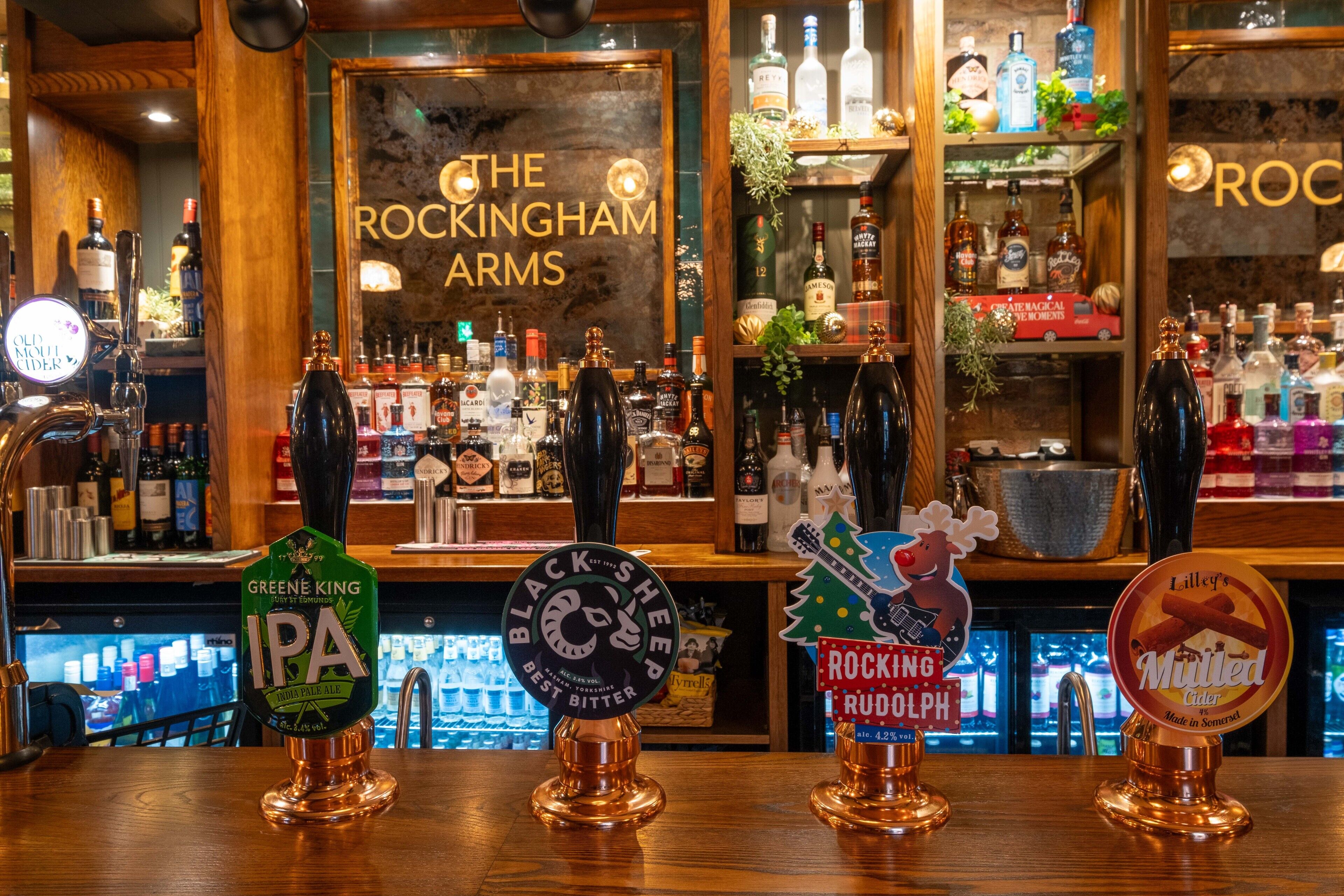 Un bar con varias toberas, incluyendo Greene King IPA y Black Sheep Best Bitter. En el fondo, se ve un letrero que dice "The Rockingham Arms".