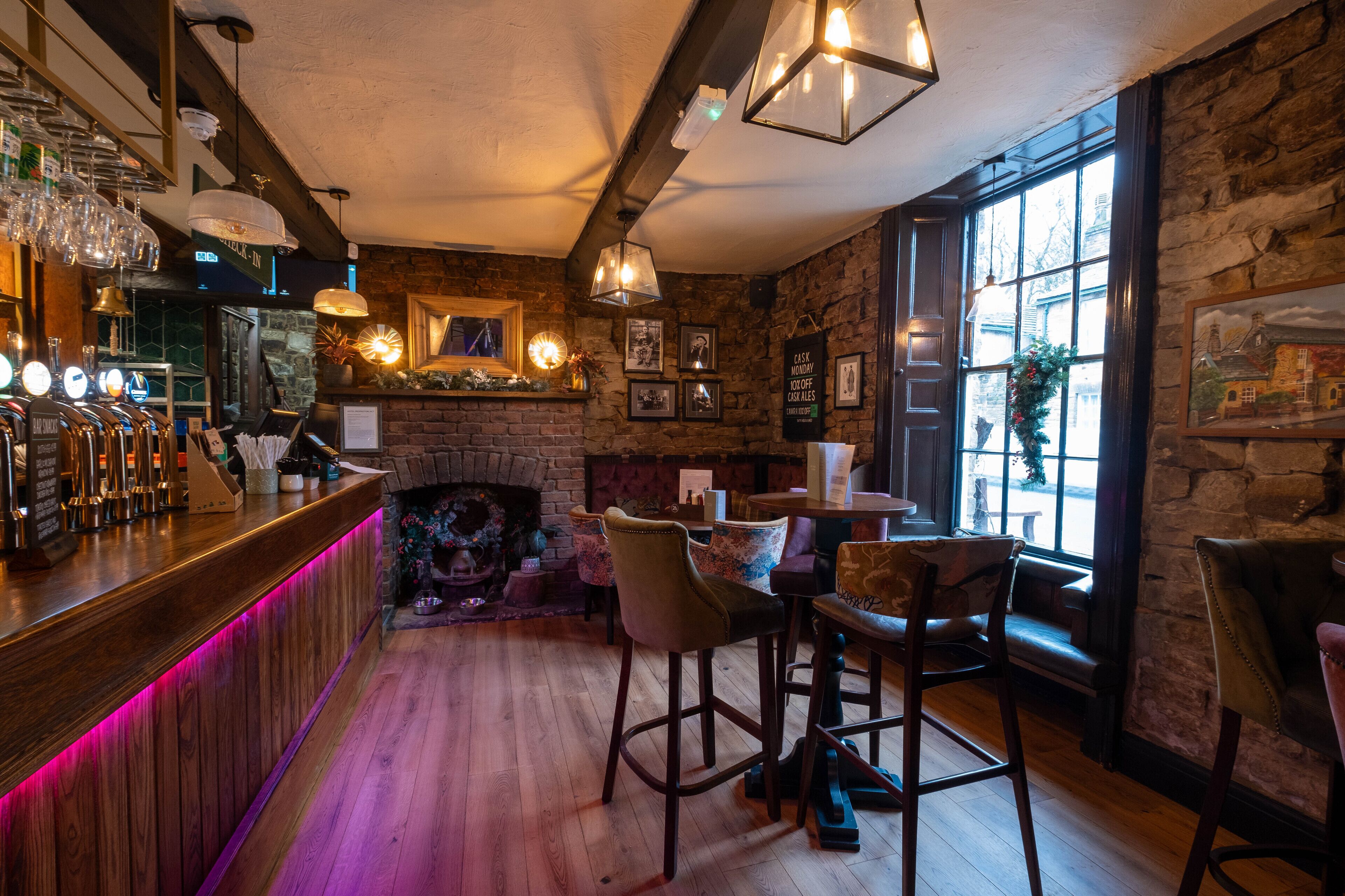 A cozy bar area with a wooden counter, bar stools, and a fireplace.