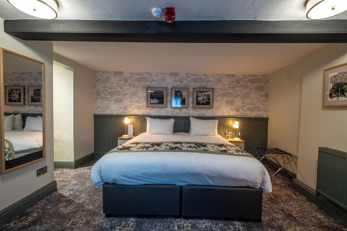 A modern hotel room with a large bed, two bedside lamps, a mirror, and a radiator.