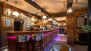 Un espace bar avec un comptoir en bois, des tabourets et des luminaires suspendus. On y trouve des panneaux indiquant les en-cas proposés au bar, ainsi qu'un menu.