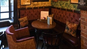 Un coin repas chaleureux avec une table ronde, des sièges confortables et un mur de briques orné de tableaux encadrés et d’assiettes décoratives.