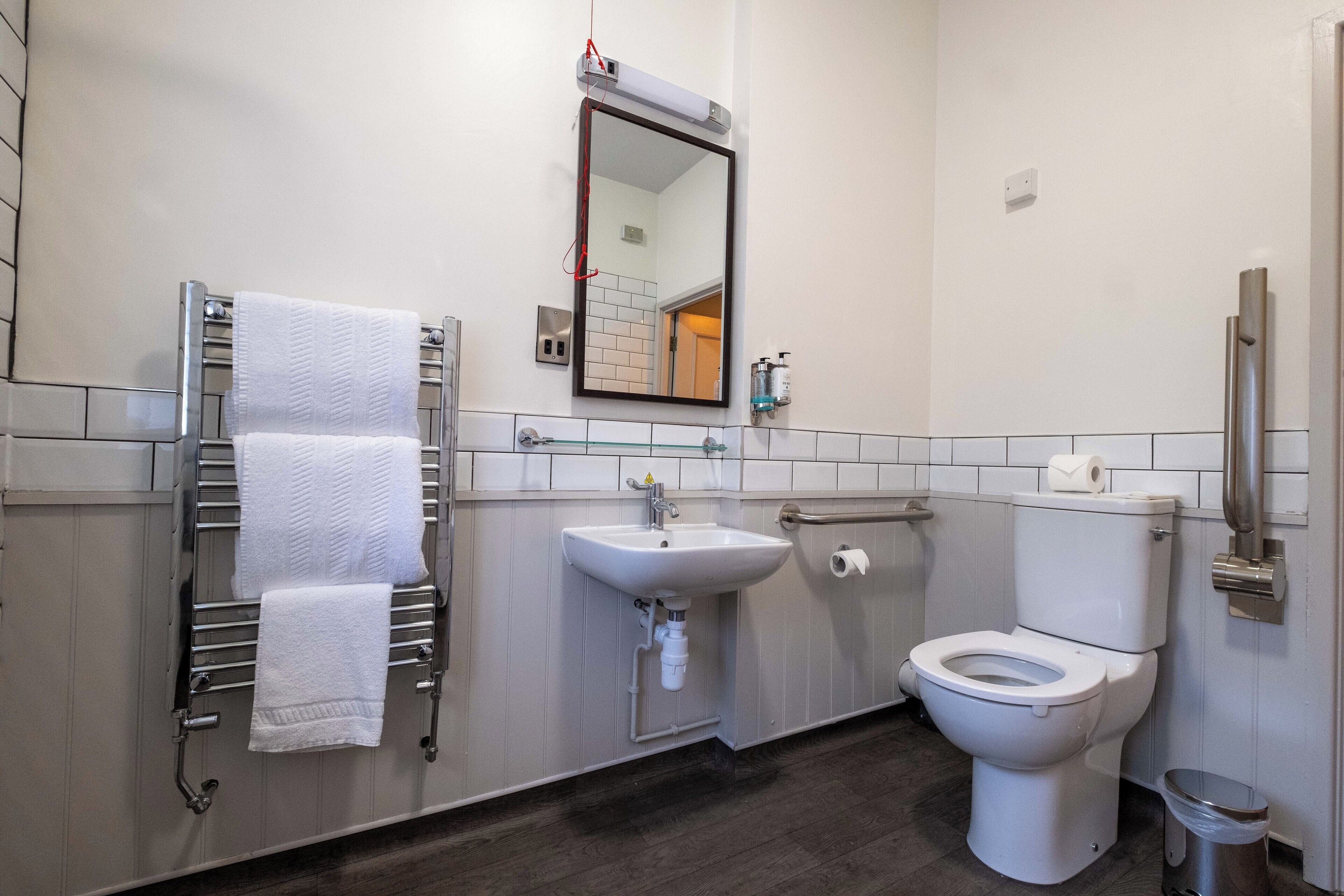 A modern bathroom with a white sink, a toilet, a towel rack with white towels, a mirror, and a trash bin.