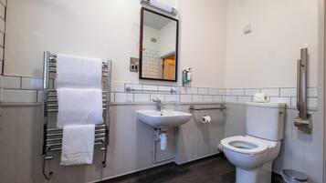 A modern bathroom with a white sink, a toilet, a towel rack with white towels, a mirror, and a trash bin.