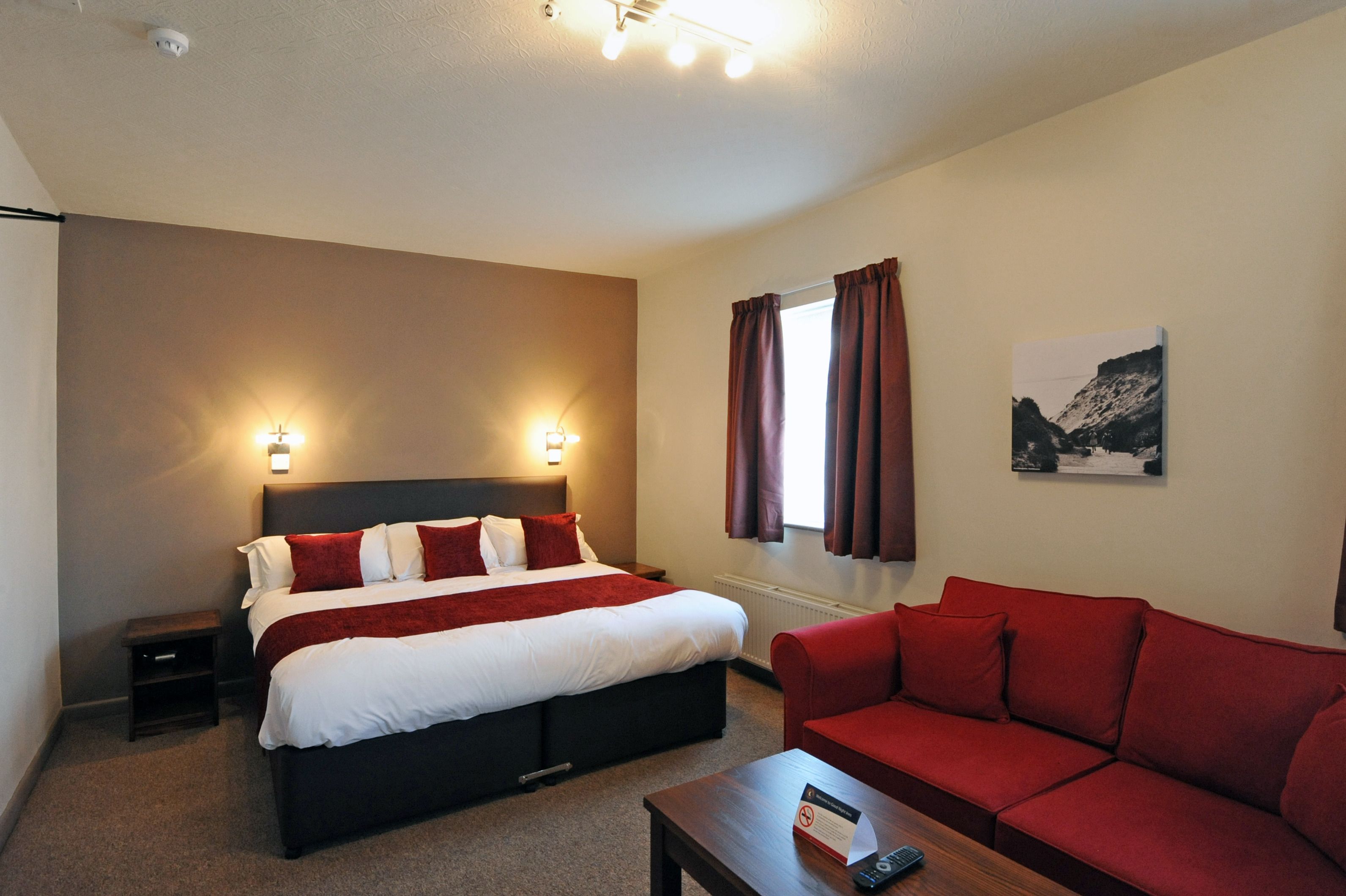 A hotel room with a bed, a red sofa, a small table, and a painting on the wall.