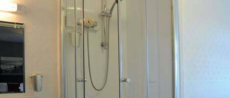 A glass-enclosed shower with a handheld showerhead, a white sink, and a small step stool.