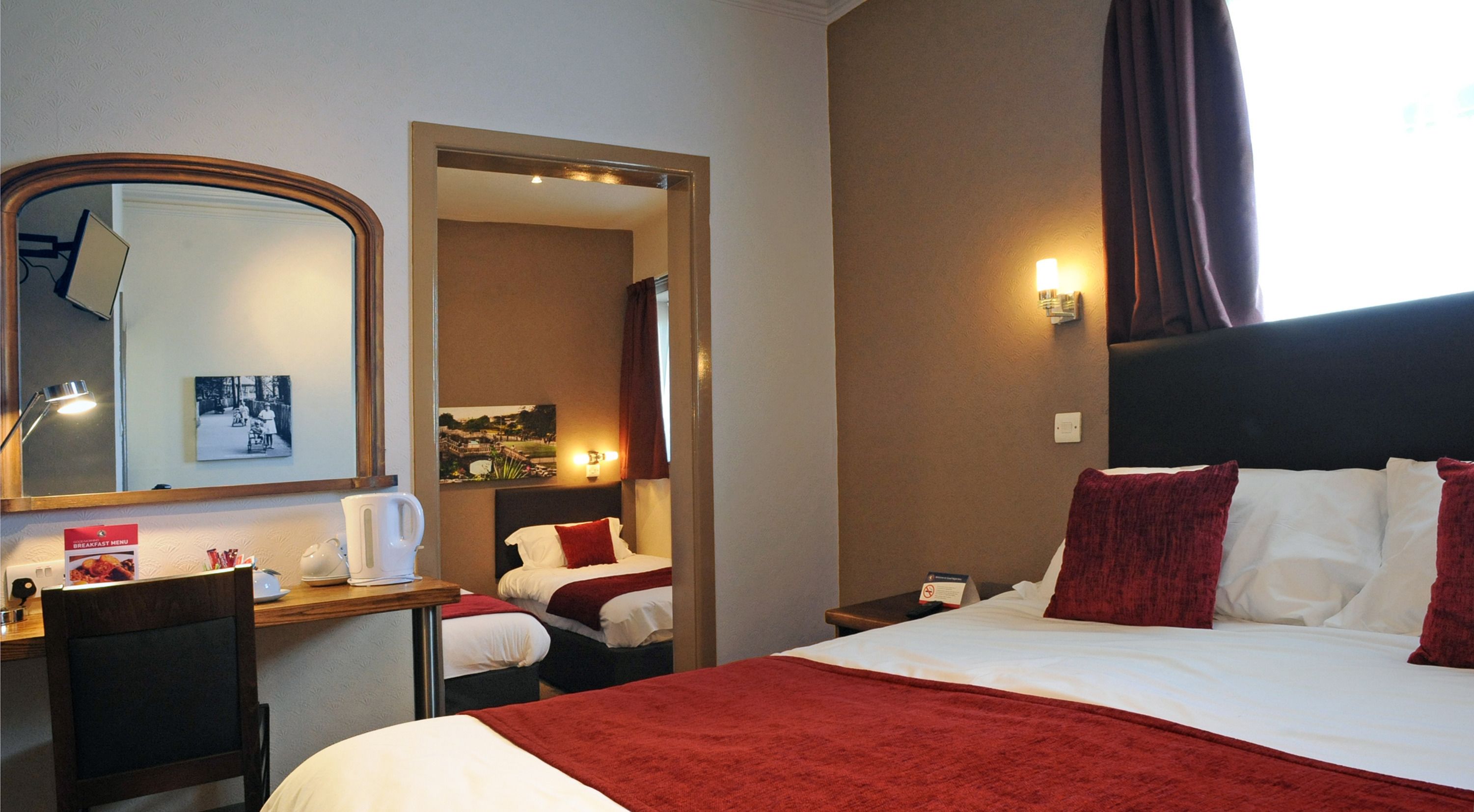 A hotel room with a large bed, a desk with a chair, a mirror, and a nightstand with a lamp.
