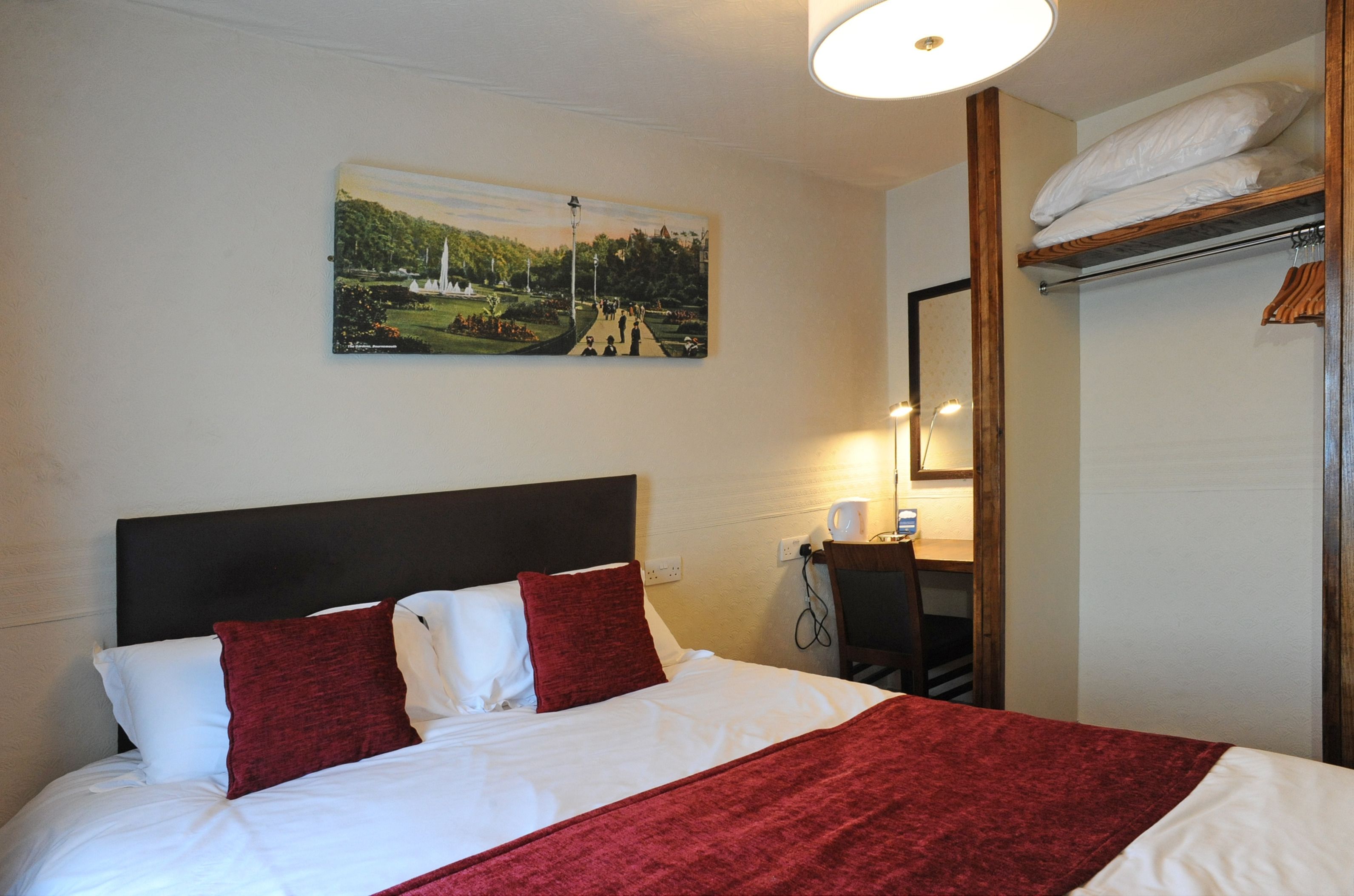 Ein Hotelzimmer mit einem Bett, einem Landschaftsbild, einem Schreibtisch mit Lampe und einem Kleiderschrank.