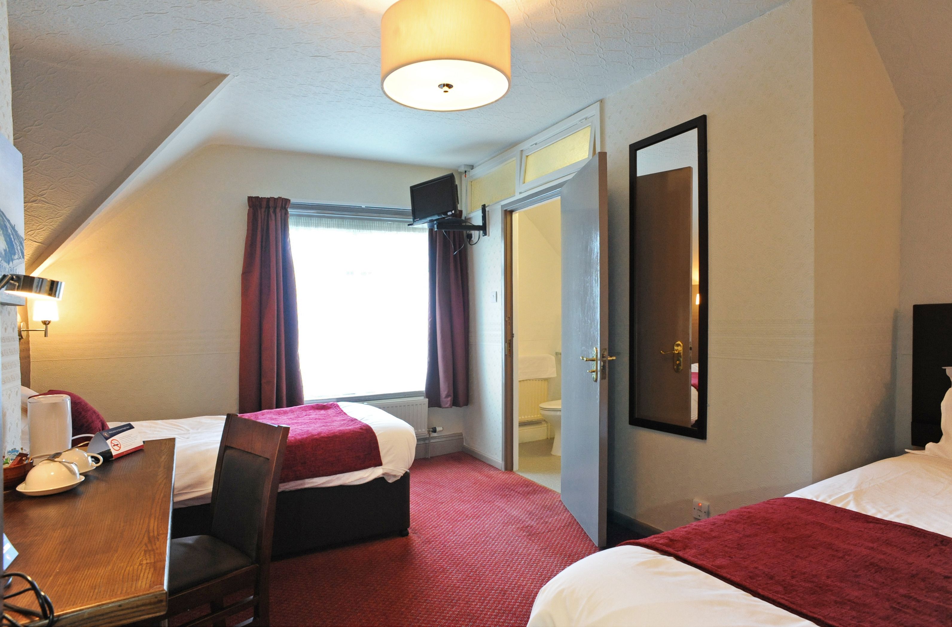 A hotel room with two beds, a desk with a chair, a television, and a bathroom visible through an open door.