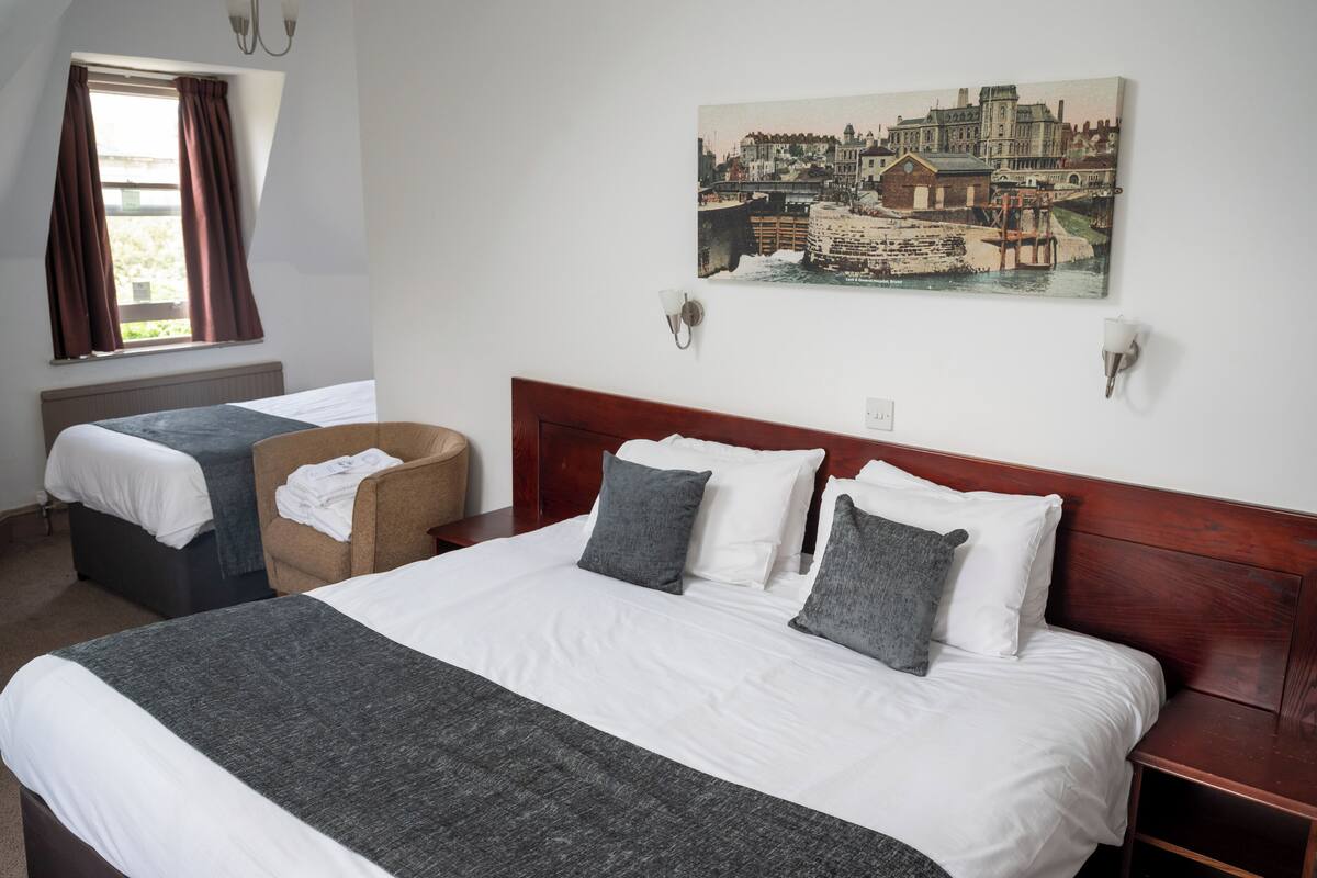 Een hotelkamer met een groot bed, een stoel, een klein tafeltje en een schilderij aan de muur.