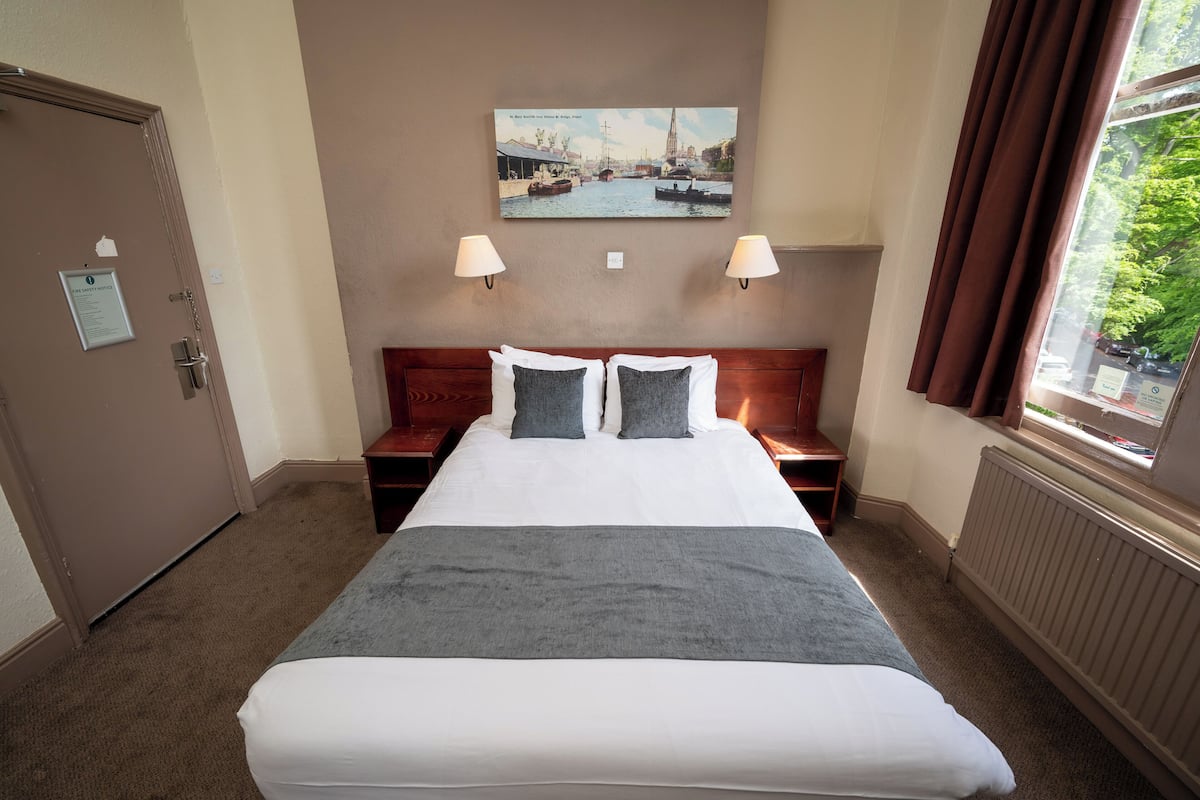 Hotelkamer met een groot bed, twee nachtkastjes, een raam met gordijnen en een aan de muur hangend schilderij.