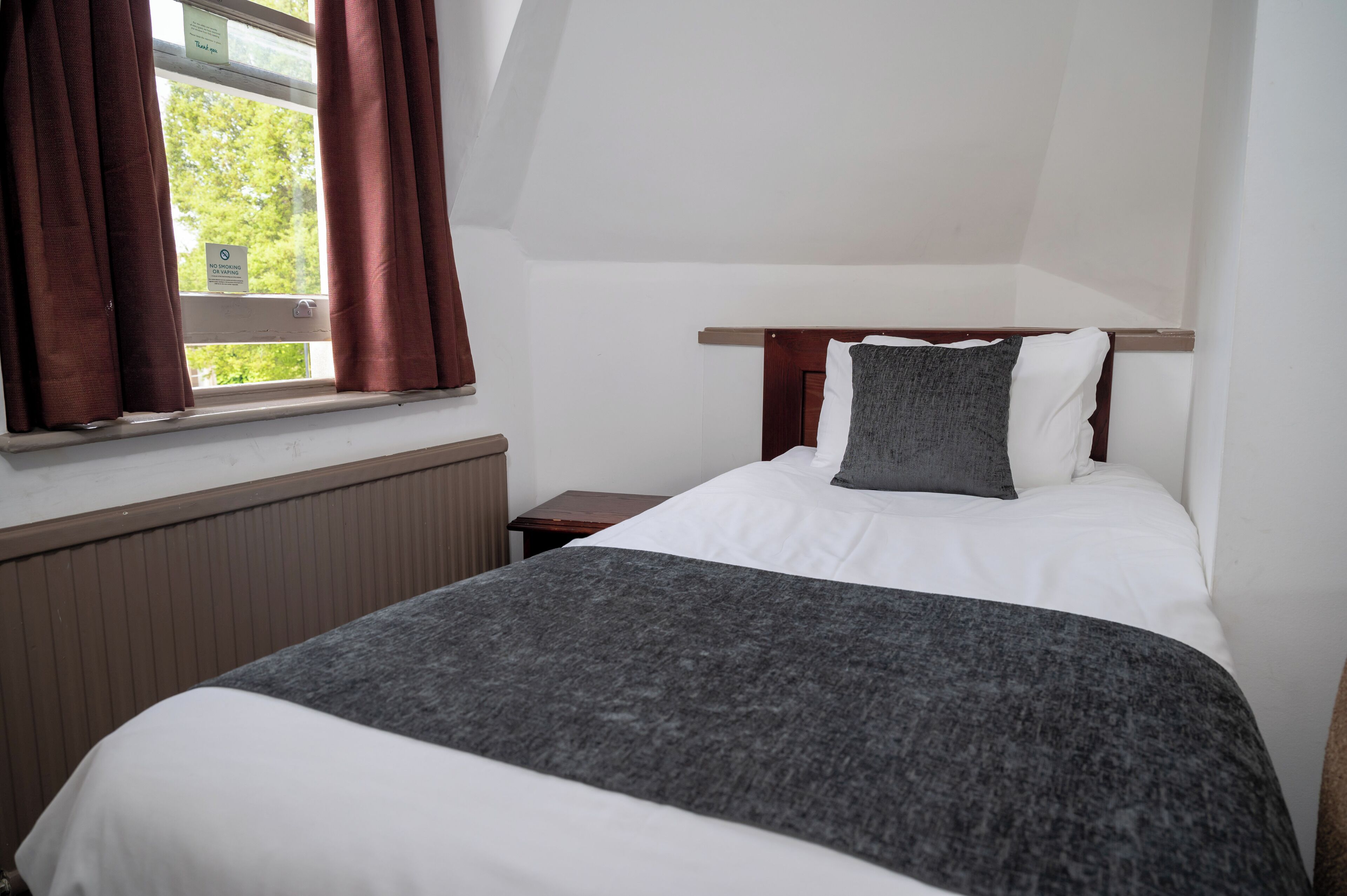 A bedroom with a bed, a nightstand, a window with curtains, and a view of trees outside.