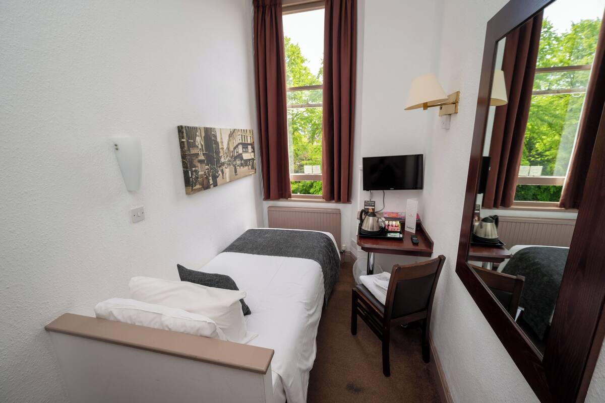 Hotelkamer met twee bedden, een bureau met een computer, een stoel en een raam met gordijnen.
