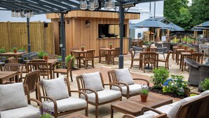 An outdoor patio area with wooden furniture, including tables and chairs, and a bar area with a wooden counter and bar stools.