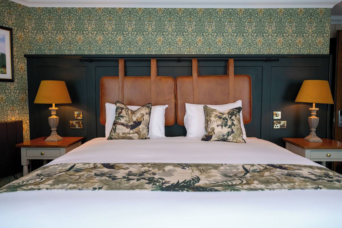 Une chambre d’hôtel avec un grand lit, deux tables de chevet, une tête de lit en bois et un papier peint à motifs.