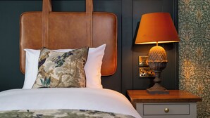 A neatly made bed with a floral pillow and a wooden nightstand with a lamp.