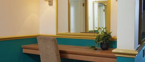 A bathroom with a wooden bench, a chair, a potted plant, and a mirror with wall sconces.