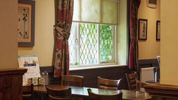 A dining area with a table and chairs, a window with a view of greenery, and a menu on the wall.