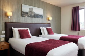 A hotel room with two beds, a nightstand, a lamp, a painting of a cathedral, and a window with curtains. - Windmill Farm by Greene King Inns (Lincoln)