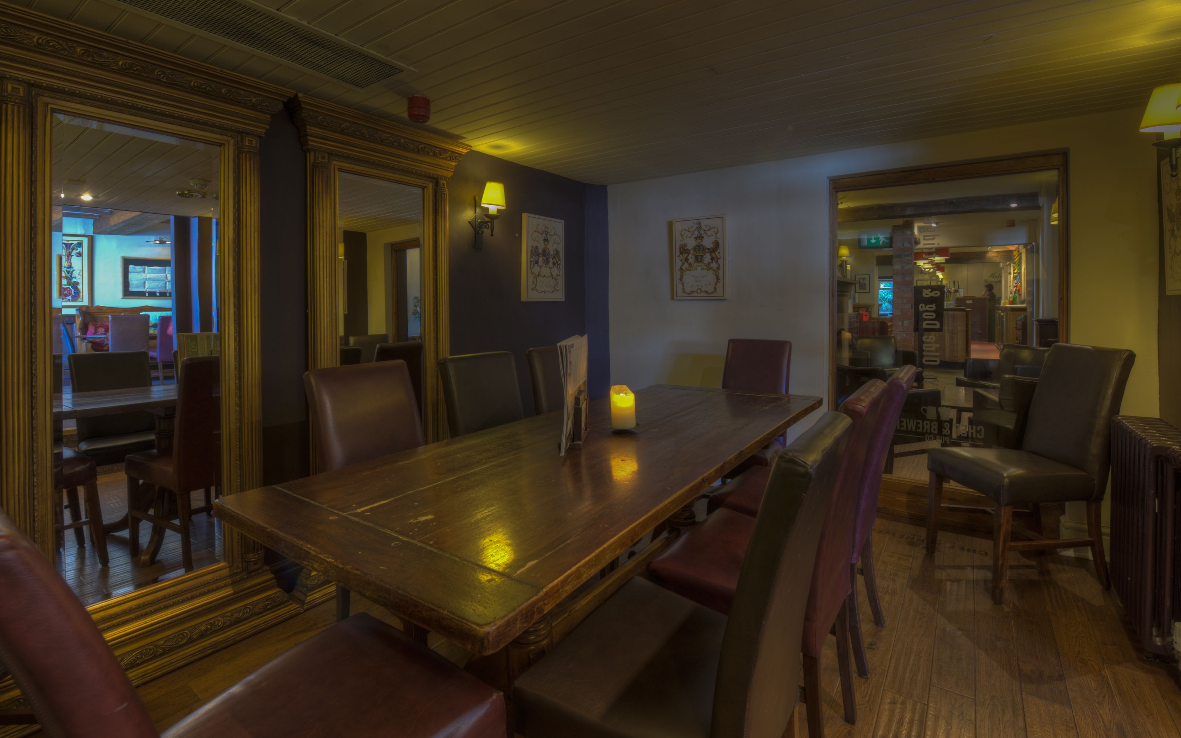 A dining area with a wooden table and chairs, a lit candle, and framed artwork on the walls.