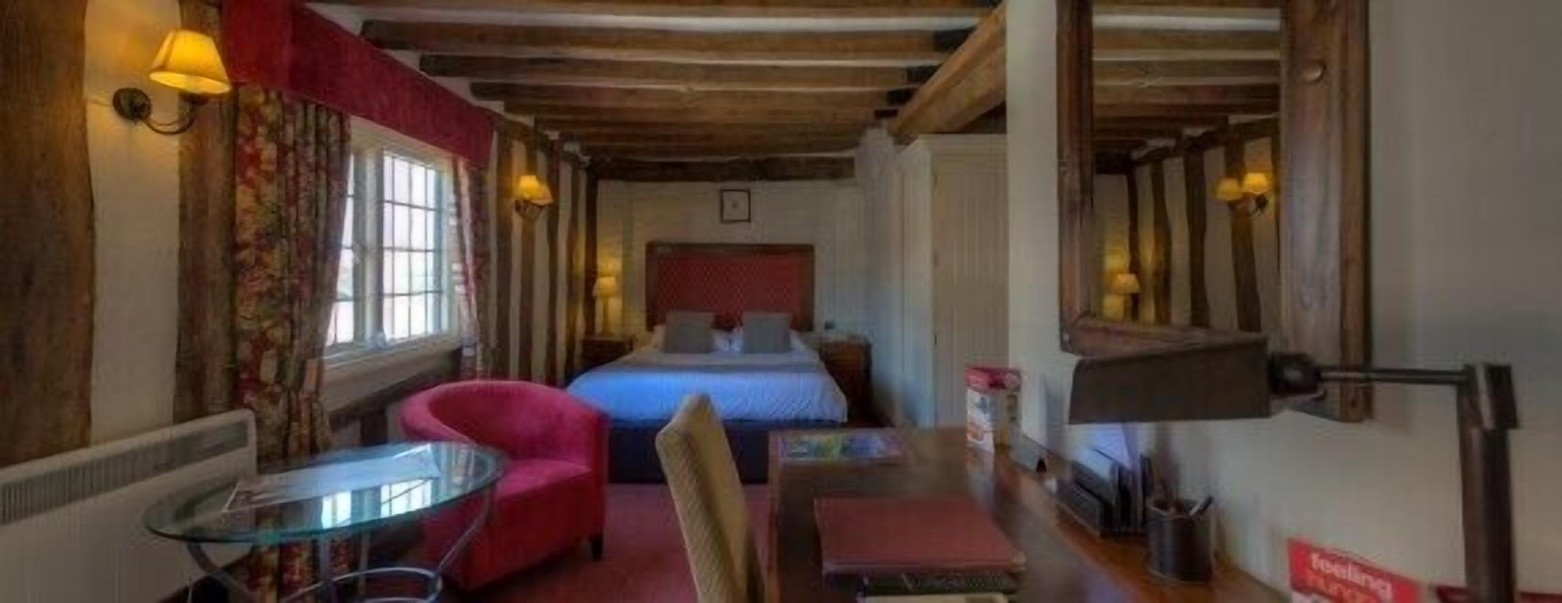 A cozy room with a bed, a red armchair, a small table, and a lamp.
