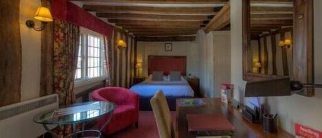 A cozy room with a bed, a red armchair, a small table, and a lamp.