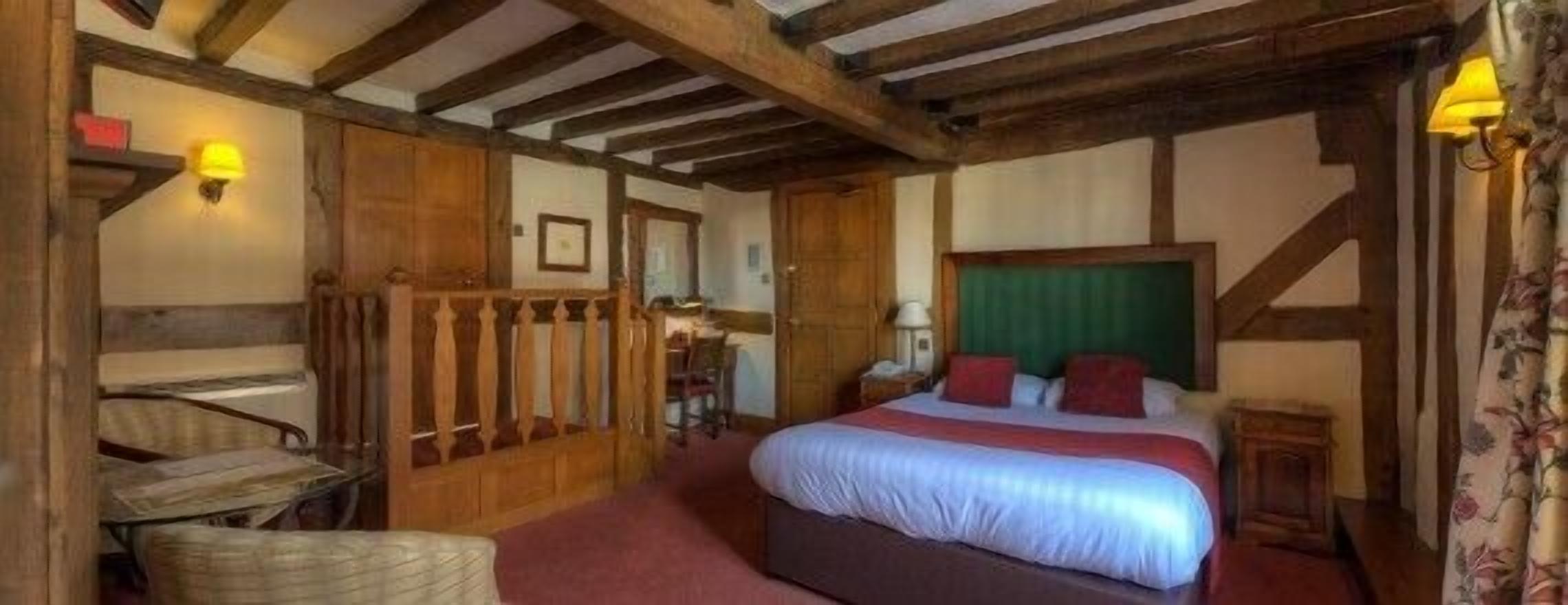 A traditional room with exposed wooden beams, a bed with red and white bedding, a small table, and a chair.